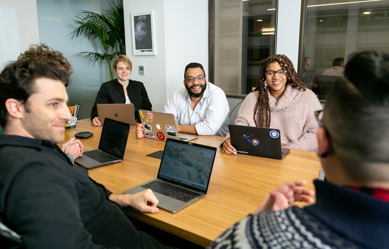 four people all on laptops, two men and two women, listen to person talking in a board meeting